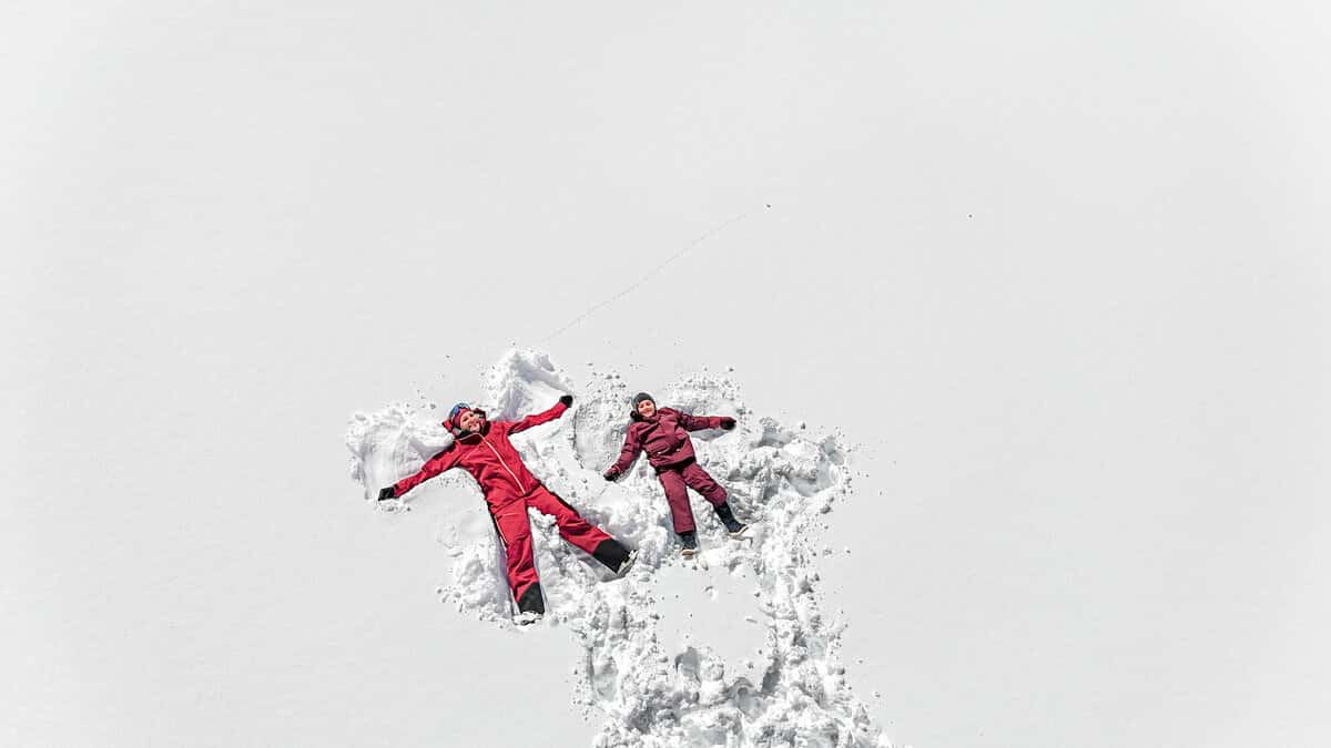 Mutter und Kind machen lachend Schnee-Engel im frischen Pulverschnee, von oben fotografiert